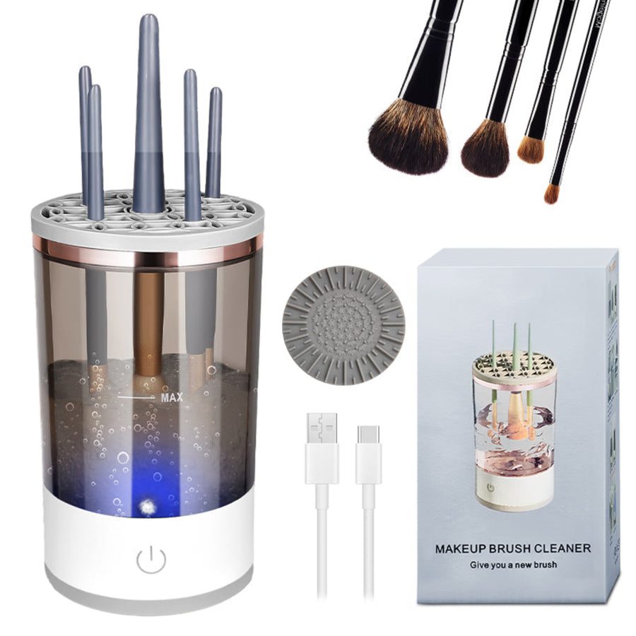 A makeup brush cleaner kit shown on a white background, including a cylindrical transparent cleaner device with multiple upright slots, several makeup brushes, a round cleaning pad, two white charging cables, and the product box labeled 'MAKEUP BRUSH CLEANER'.