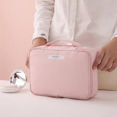 Pink makeup bag with 'MAKEUP' label held by a person, on a light pink background